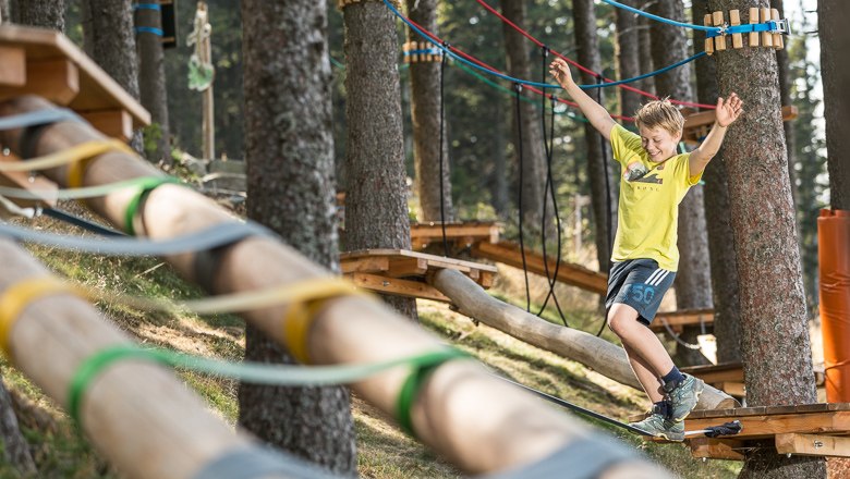 Ein Junge balanciert auf einem Seil in einem Kletterpark im Wald.