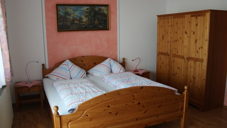 Ein Schlafzimmer mit einem Doppelbett, zwei Nachttischen, einem Kleiderschrank und einem Gemälde an der Wand.