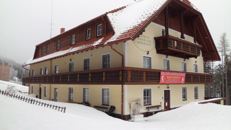 A large, snow-covered building with wooden cladding and balconies, surrounded by snow.