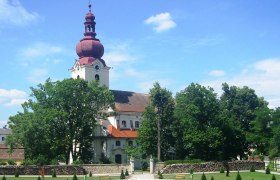 Barockkirche mit rotem Turm und Garten im Vordergrund.
